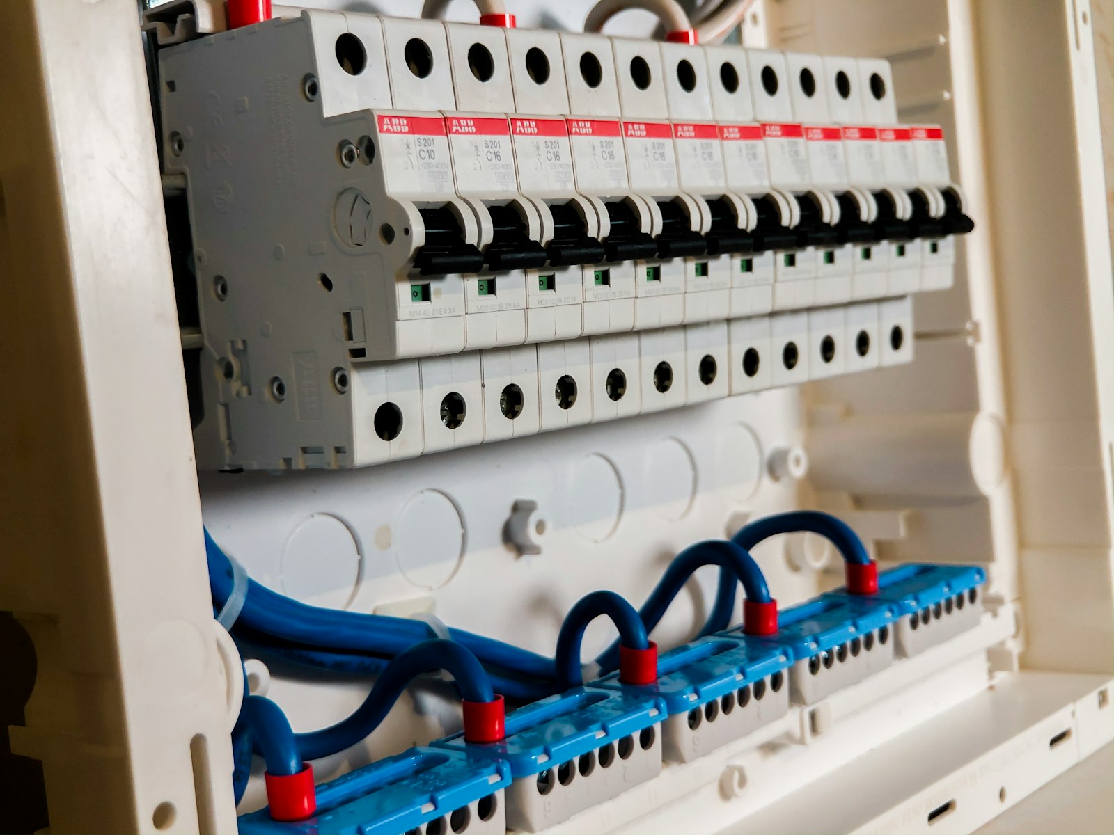 Een geopende groepenkast met een rij ABB-installatieautomaten op een DIN-rail en een blauwe kamrail eronder